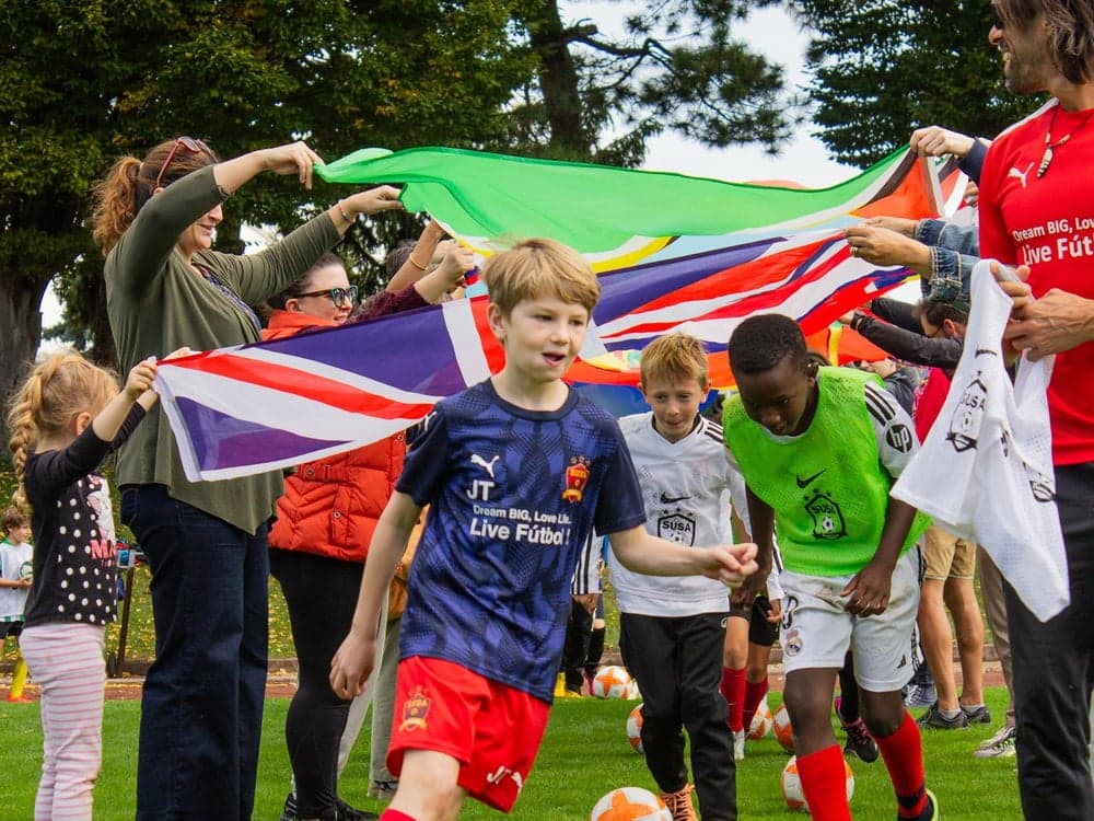 Children playing under a large international flag held by coaches